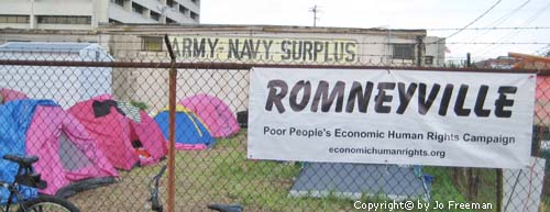 Romneyville sign on a chainlink fence, behind are many colorful camping tents near an army navy surplus store