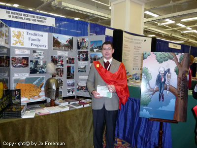 a young man in a bright red sash and a suit stands in front of several curious dioramas